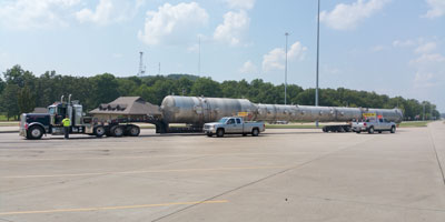 An oversized load parked inside a rest area flanked by two pilot car vehicles.