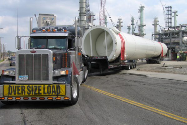 A oversize rig backs into a job site hauling a large surge drum on 13 axles.