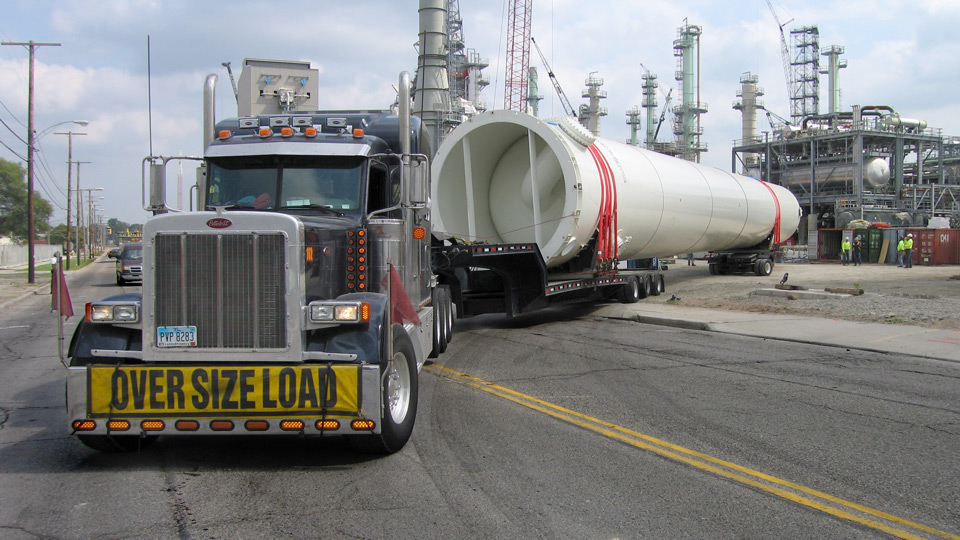 A oversize rig backs into a job site hauling a large surge drum on 13 axles.