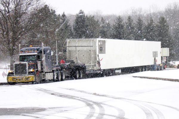 A oversive load makes its way into a rest area through harsh winter conditions.