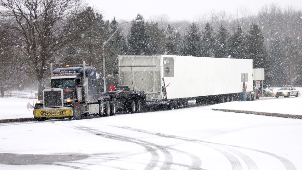A oversive load makes its way into a rest area through harsh winter conditions.