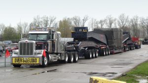 A 20 axle trailer, loaded with and injection mold machine clamp and sitting in a parking lot on an overcast day.