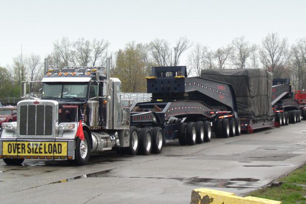 A 20 axle trailer, loaded with and injection mold machine clamp and sitting in a parking lot on an overcast day.