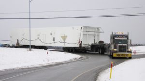 A truck hauling a oversize cold box manuvers around a turn using a 6 axle steerable dolly.