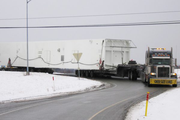 A truck hauling a oversize cold box manuvers around a turn using a 6 axle steerable dolly.