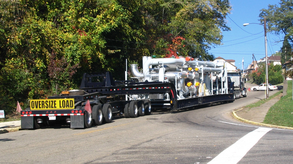A superload makes its way up a hill on narrow city streets.