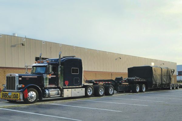 A 11 axle trailer sitting in Michigan at an empty parking lot loaded with an injection mold machine clamp.