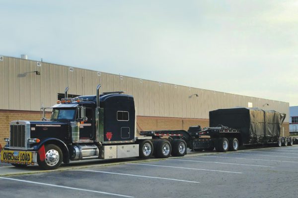 A 11 axle trailer sitting in Michigan at an empty parking lot loaded with an injection mold machine clamp.