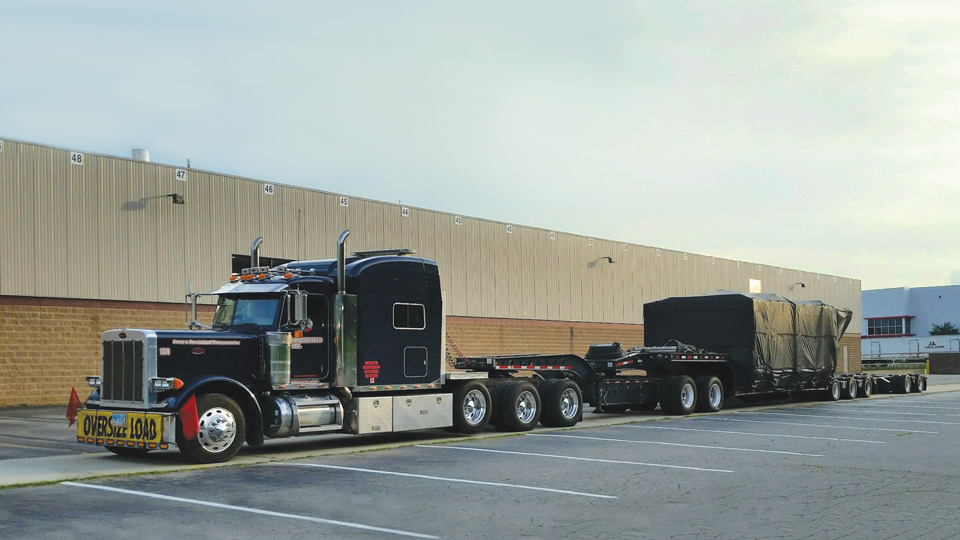 A 11 axle trailer sitting in Michigan at an empty parking lot loaded with an injection mold machine clamp.