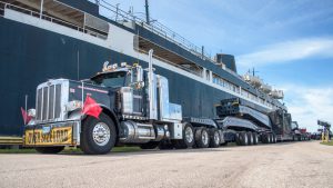 A 20 axle rig parked alongside a large ship.