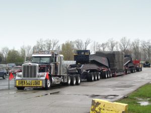 A 20 axle trailer, loaded with and injection mold machine clamp and sitting in a parking lot on an overcast day.